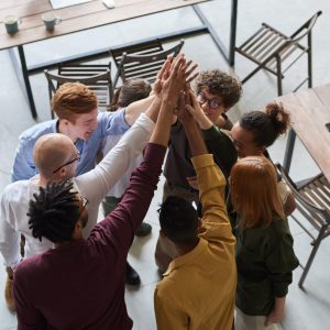 A group of eight individuals gathered in a circle and raising their hands together in a team motion.