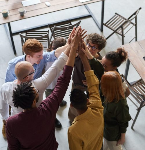 A group of eight individuals gathered in a circle and raising their hands together in a team motion.