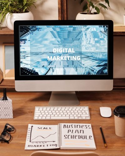 A computer with a screen that displays the words "digital marketing" and a notepad on the desk.